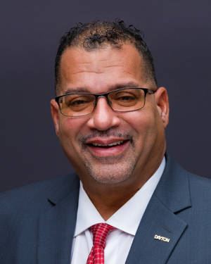 Commissioner Chris Shaw smiling in a grey suit with a gold pin spelling out Dayton on it.