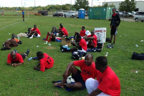 Team in red jerseys on sideline at Dayton World Soccer Games.