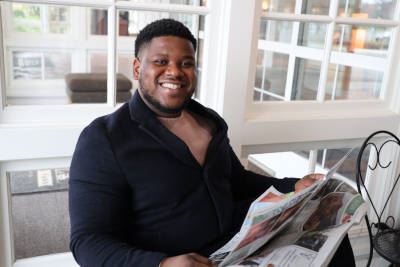 Fabrice Juin smiling at camera while reading a newspaper at a cafe at Carillon Historical Park.